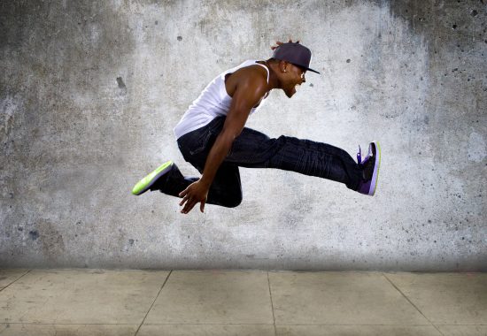 Black urban hip hop dancer jumping high on a concrete background