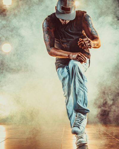 Young cool man break dancing in club with lights and smoke. Tattoo on body.