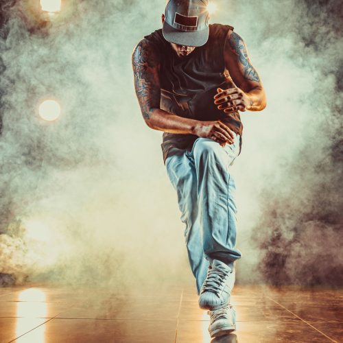 Young cool man break dancing in club with lights and smoke. Tattoo on body.