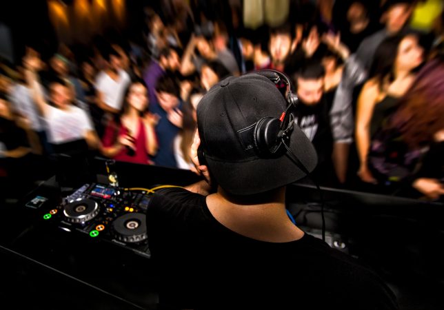 DJ with headphone and dj set at night club party. People at the