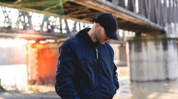 portrait of young rapper posing under a metal bridge in the suburbs