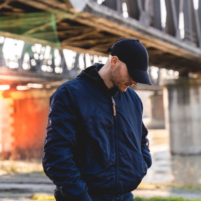 portrait of young rapper posing under a metal bridge in the suburbs