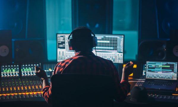 Artist, Musician, Audio Engineer, Producer in Music Record Studio, Uses Control Desk with Computer Screen showing Software UI with Song Playing. Success with Raised Hands, Dances. Back View.