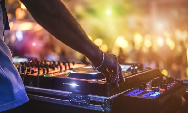 Dj mixing outdoor at beach party festival with crowd of people in background - Summer nightlife view of disco club outside - Soft focus on hand - Fun ,youth,entertainment and fest concept