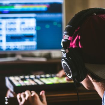 back view of sound engineer in snapback and holding headphones on head monitoring music in studio